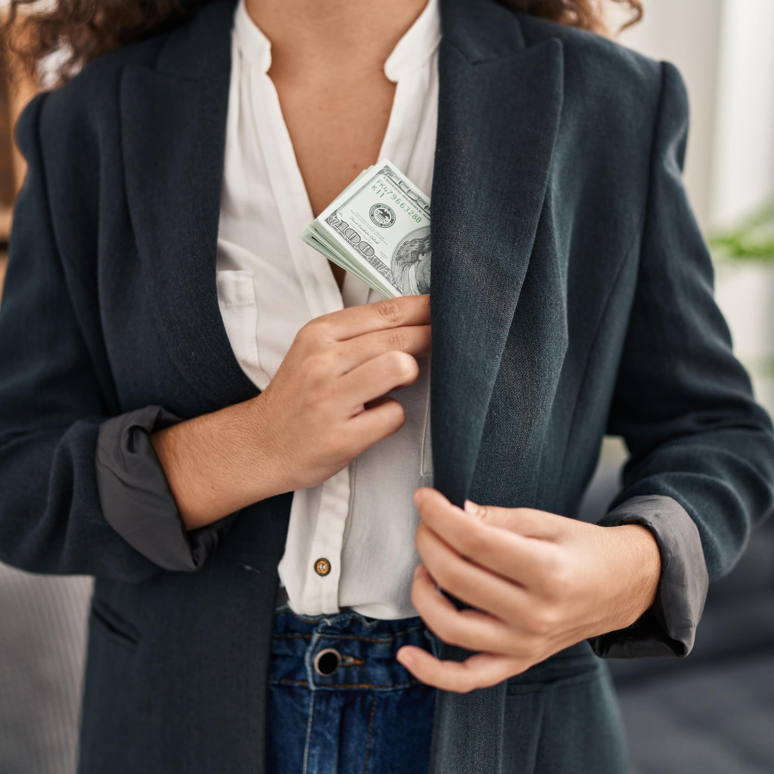 A stock image of a Latino woman putting a wad of US dollars in her pocket.
