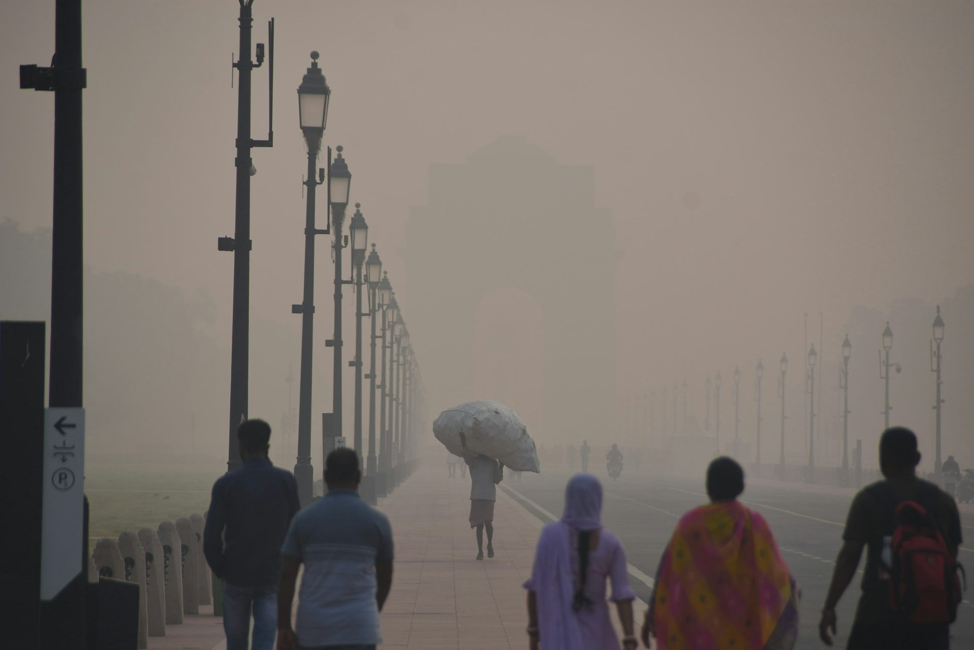 A group of people walk down a street in New Delhi that is engulfed in smog.