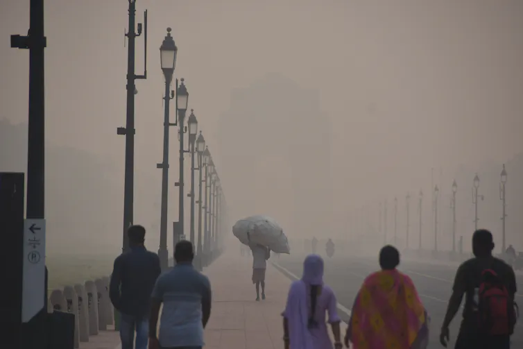 A group of people walk down a street in New Delhi that is engulfed in smog.