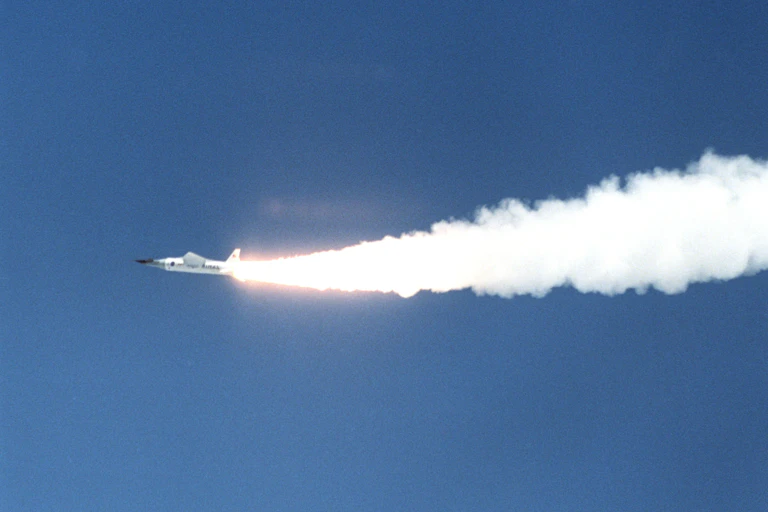 A small aircraft streaking across the sky, with a large plume of smoke coming from its exhaust.