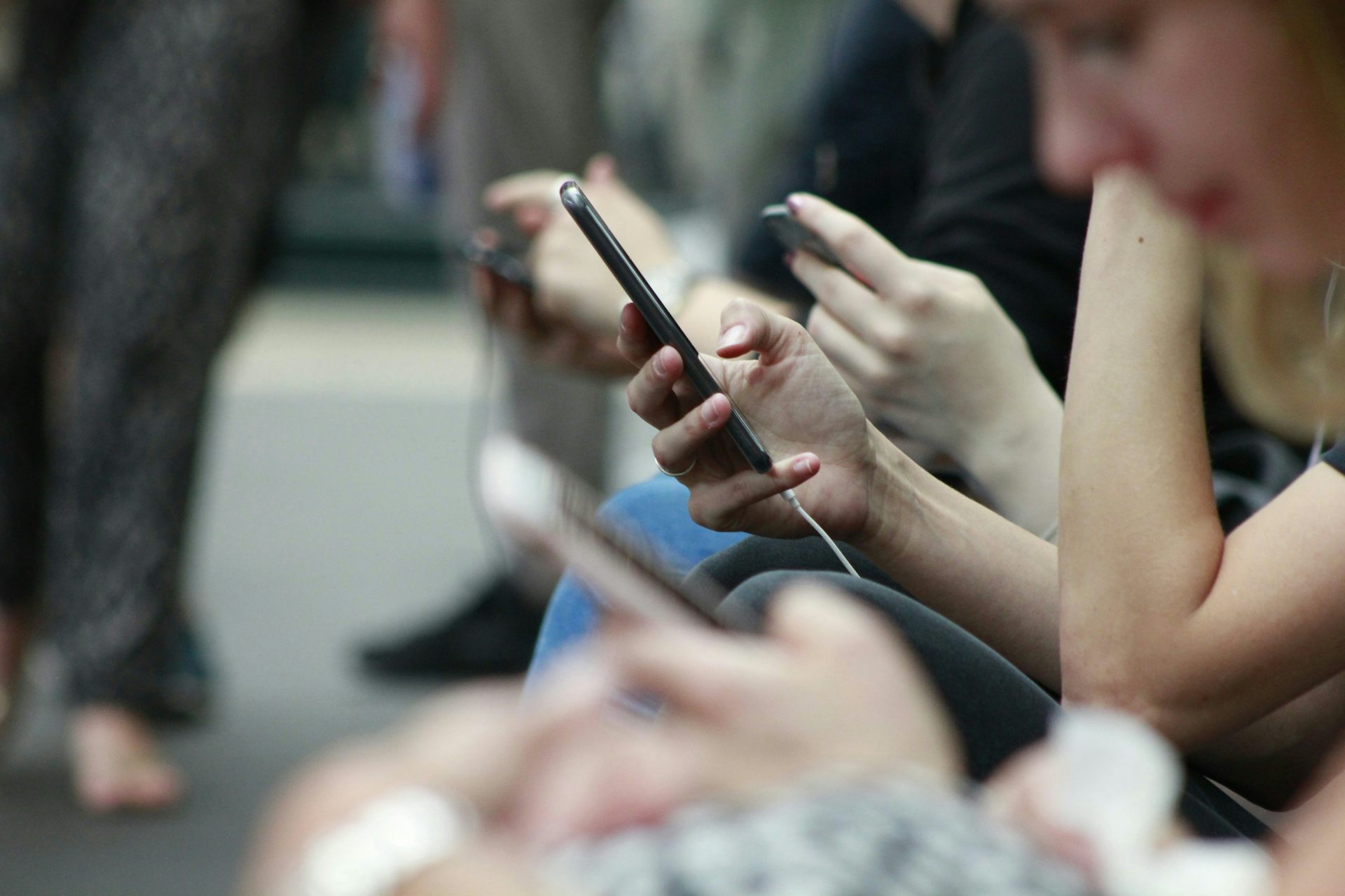Closeup of people's hands as they scroll on their phones while sitting on a bench