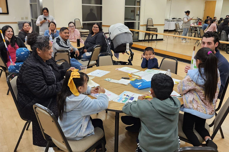 An education professor sits at a table with young children and parents.
