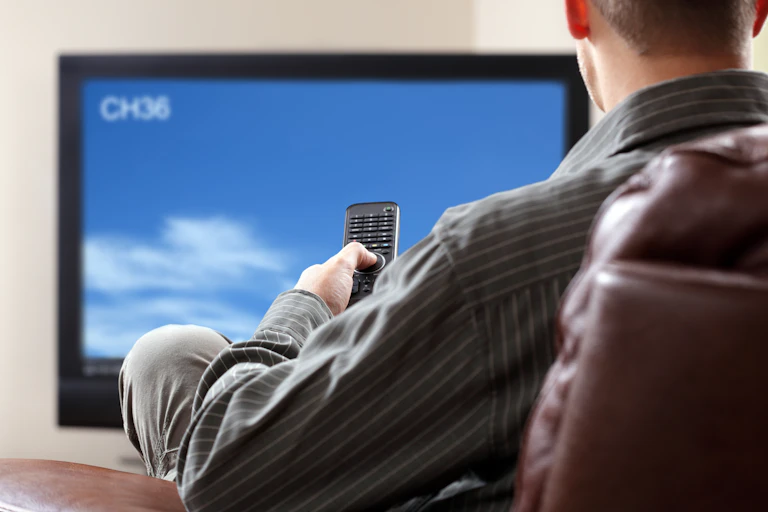 Back of a person's head as they watch tv while holding a remote