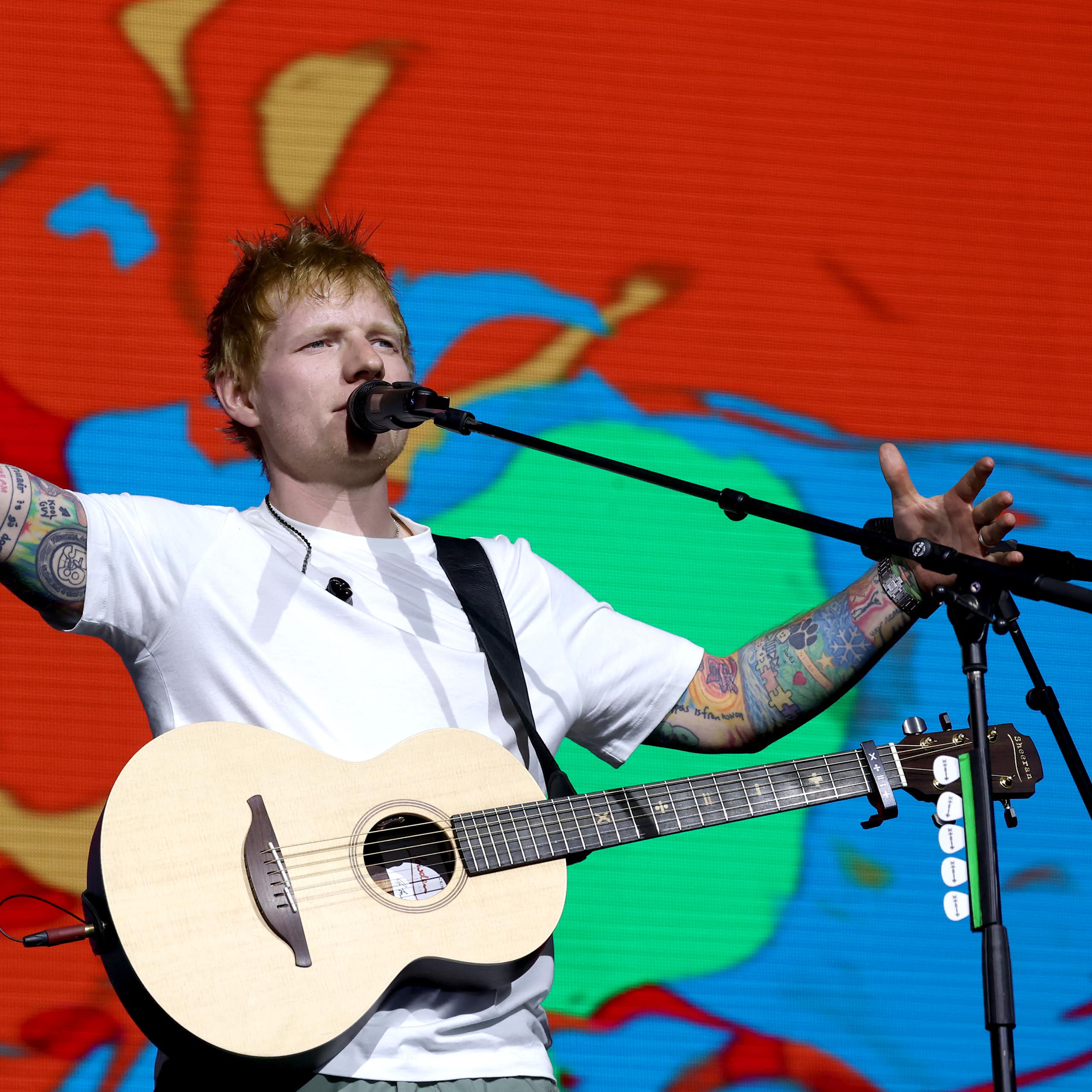 Pop star Ed Sheeran in a white t-shirt, holding a guitar and with a colourful background.