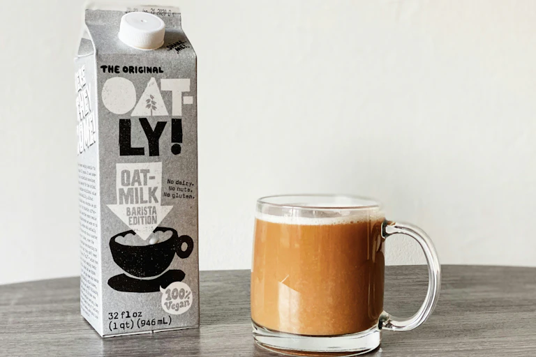 A carton of Oatly milk and mug of coffee