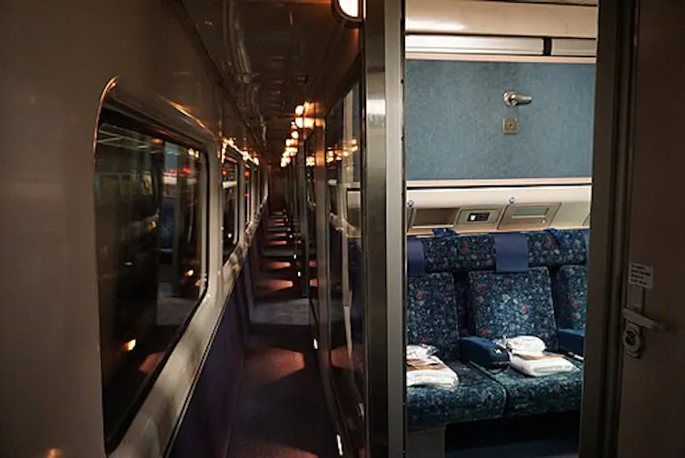 The interior of an XPT train sleeper car, showing a darkened corridor and three seats.