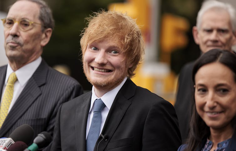 A red-hair man with fluffy hair smiles at the camera.