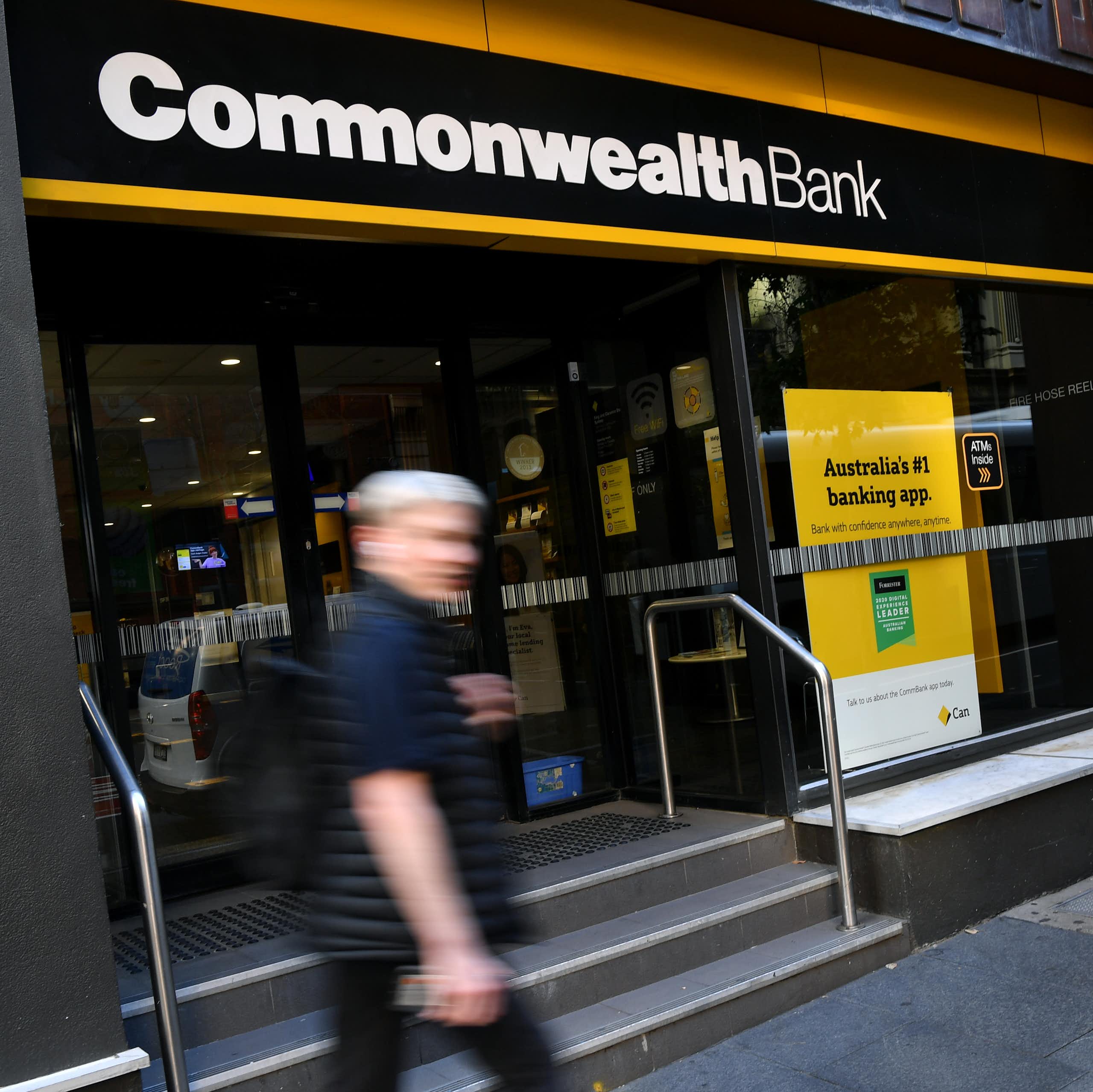 A blurred image of a person walking in front of a Commonwealth Bank branch