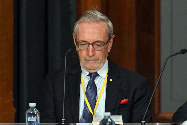 A grey-haired man with glasses looks down
