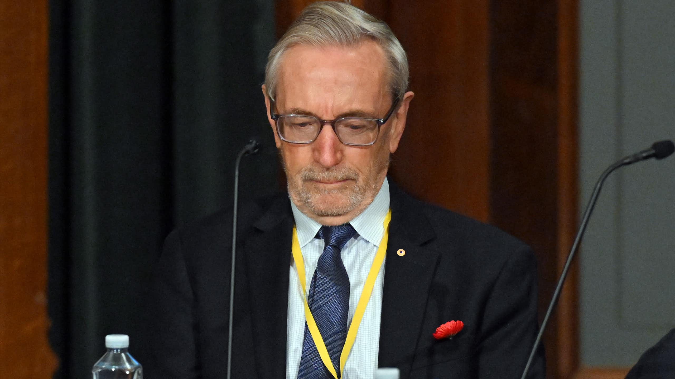 A grey-haired man with glasses looks down