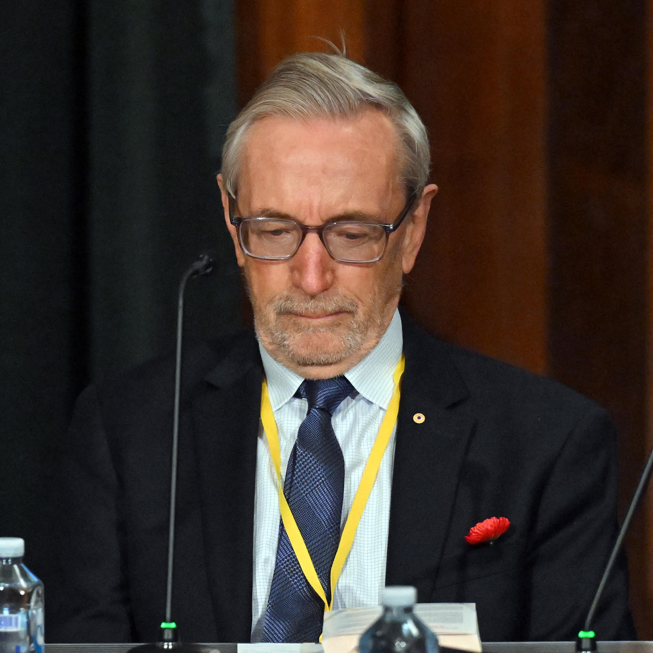 A grey-haired man with glasses looks down