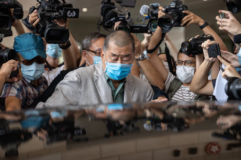 Hong Kong media mogul Jimmy Lai, wearing a mask, getting into a car surrounded by press photographers.
