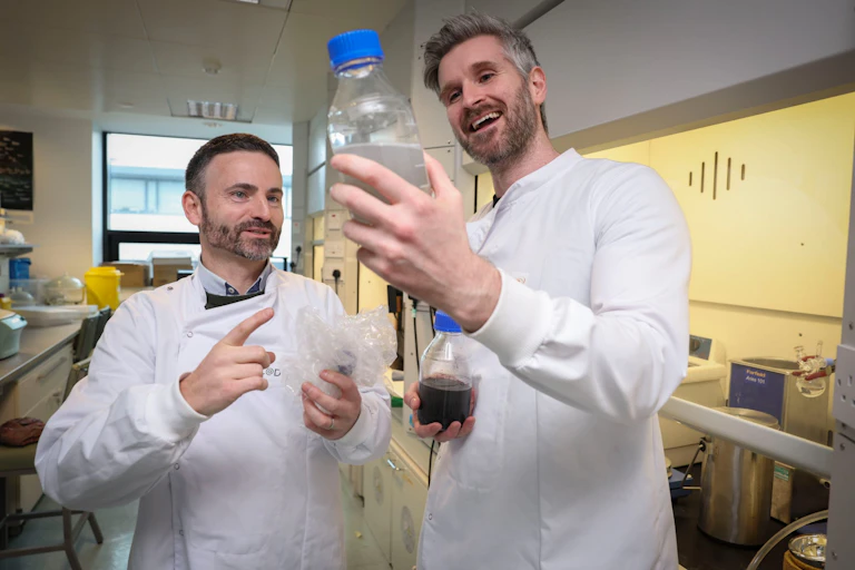 two men in white coasts in science lab holding plastic bottle