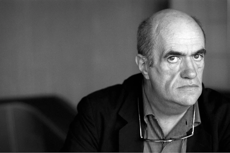 A black and white image of a sombre-looking bald man looking intently at the camera.