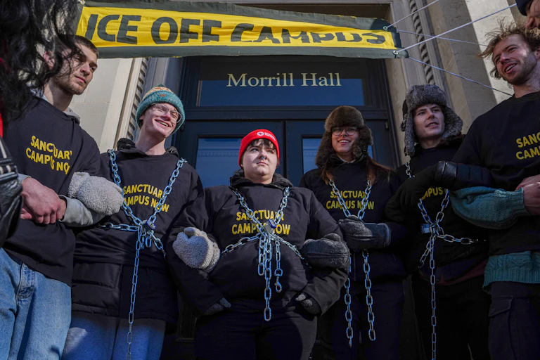 A group of students block access to a building under a banned that reads, "ICE off campus."