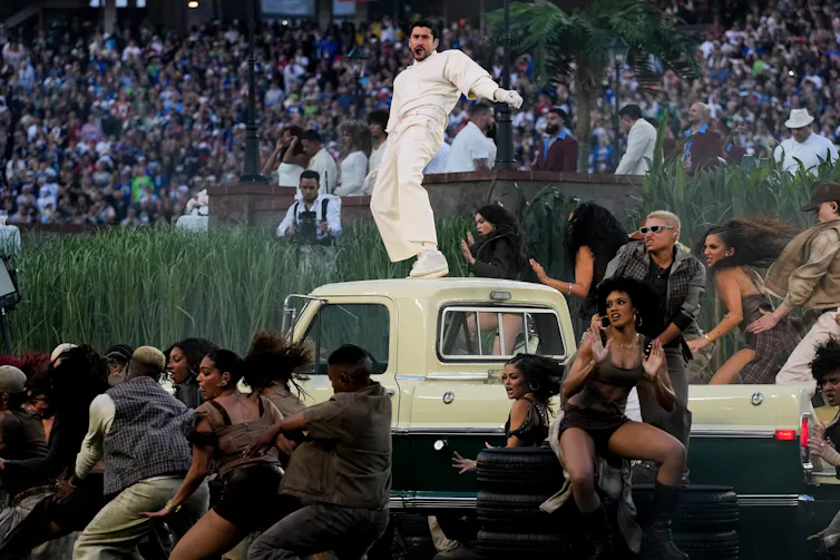 A musician dancing on the hood of a care surrounded by other dancers.