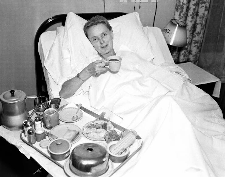 Woman holds a cup of tea while lying in a hospital bed.