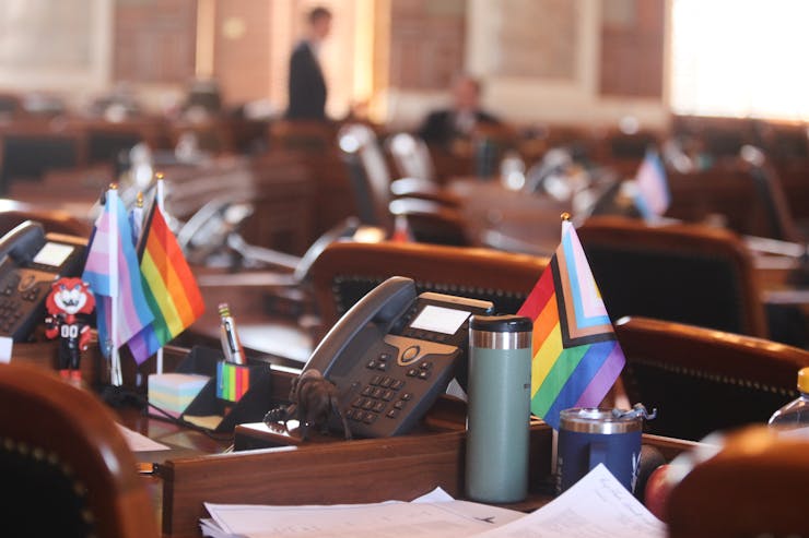 Small LGBTQ+ and trans pride flags adorn two legislators' desks