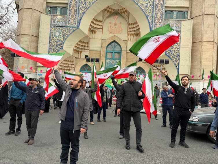 Several men wave flags in front of a building.