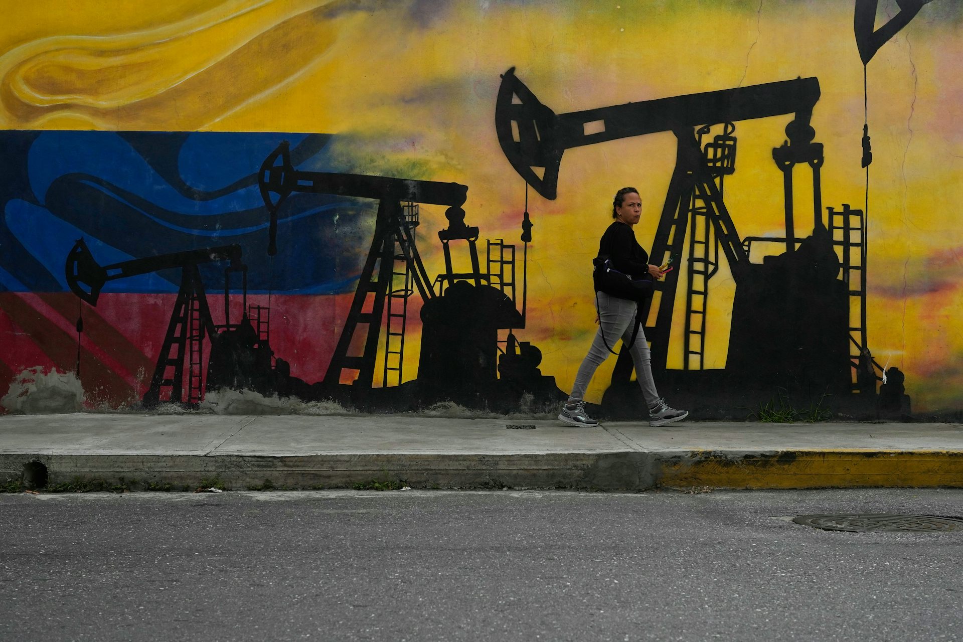 Una persona pasa junto a un mural de una plataforma petrolera con los colores de la bandera venezolana de fondo.