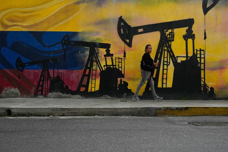 El frágil medio ambiente de Venezuela enfrenta riesgos crecientes a medida que Estados Unidos oferta petróleo y minerales críticos y expande la minería ilegal de oro. 2 Una persona pasa junto a un mural de una plataforma petrolera con los colores de la bandera venezolana de fondo.