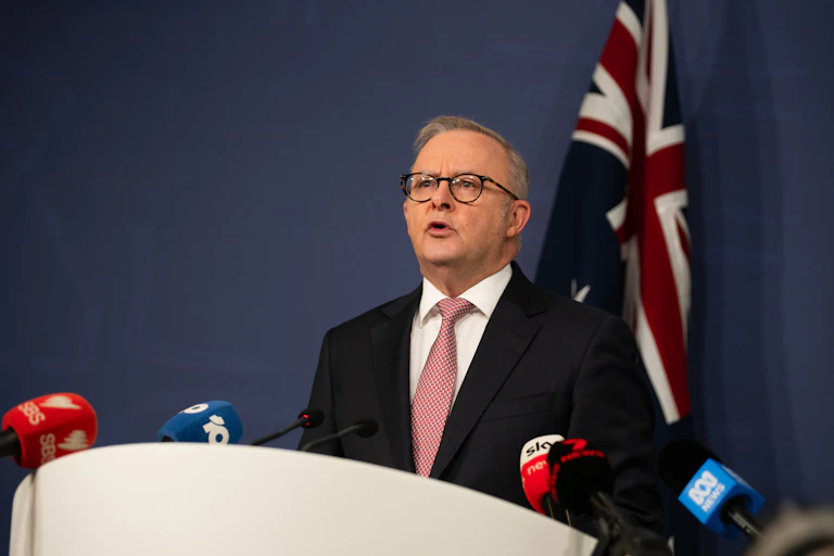 Prime Minister Anthony Albanese speaks at a press conference in front of an Australian flag.