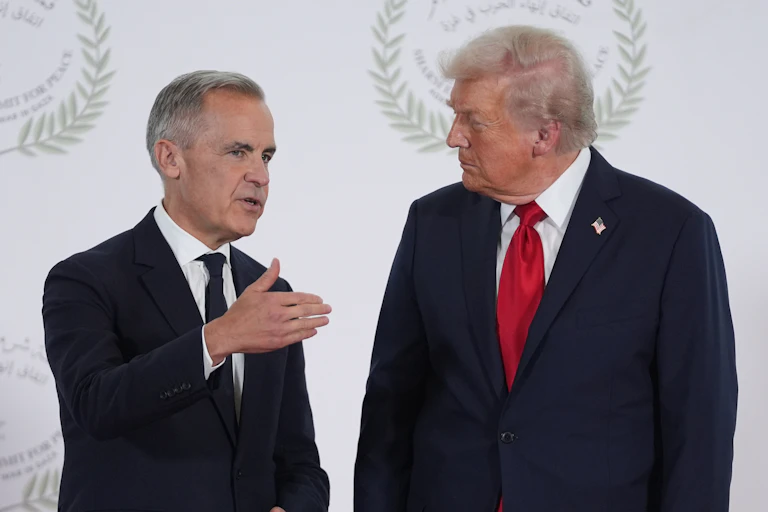 A slim man with short grey hair talks to a larger, older man with orange-hued skin and fluffy yellowish-white hair.