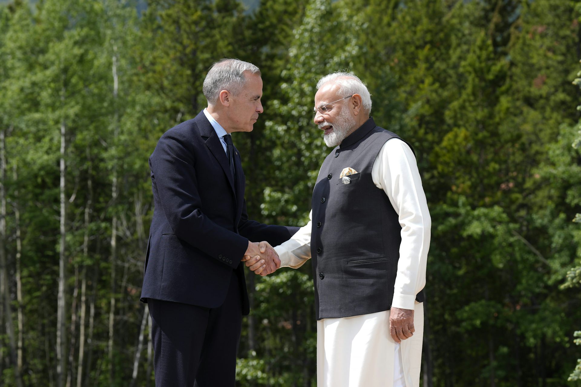 Dos hombres se dan la mano contra el fondo de árboles de hoja perenne.