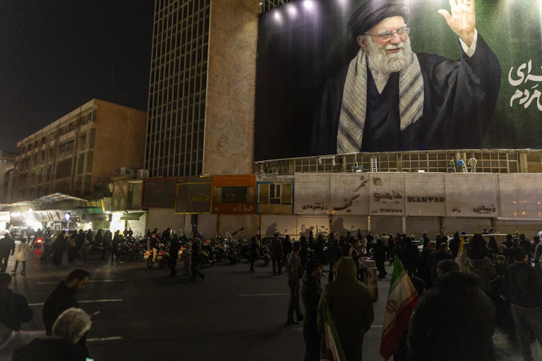 People stand in the street in front of a large banner showing a man with a beard.