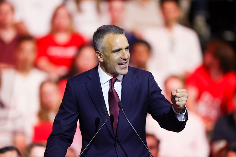 A man stands at a podium and makes a victory fist in front of a crowd.