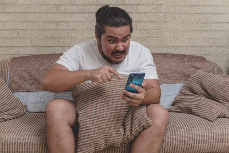 Angry person sitting on a couch pointing at phone