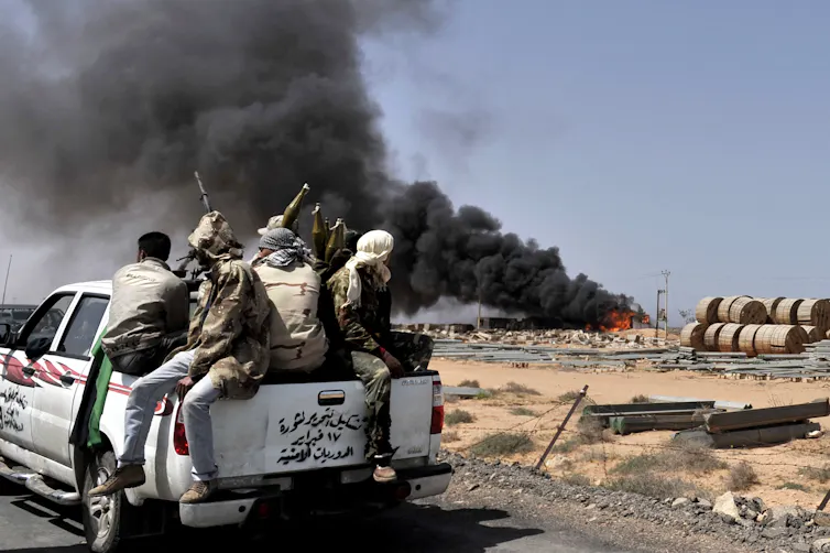 A pickup truck with soldiers drives towards a plume of smoke.