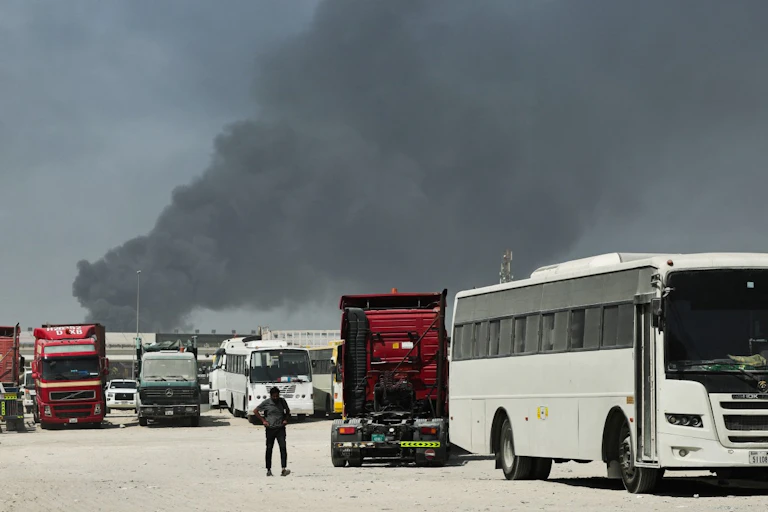 Un homme marche sur un parking tandis que de la fumée s’élève du port de Jebel Ali après une frappe iranienne à Dubaï, le 1er mars 2026.