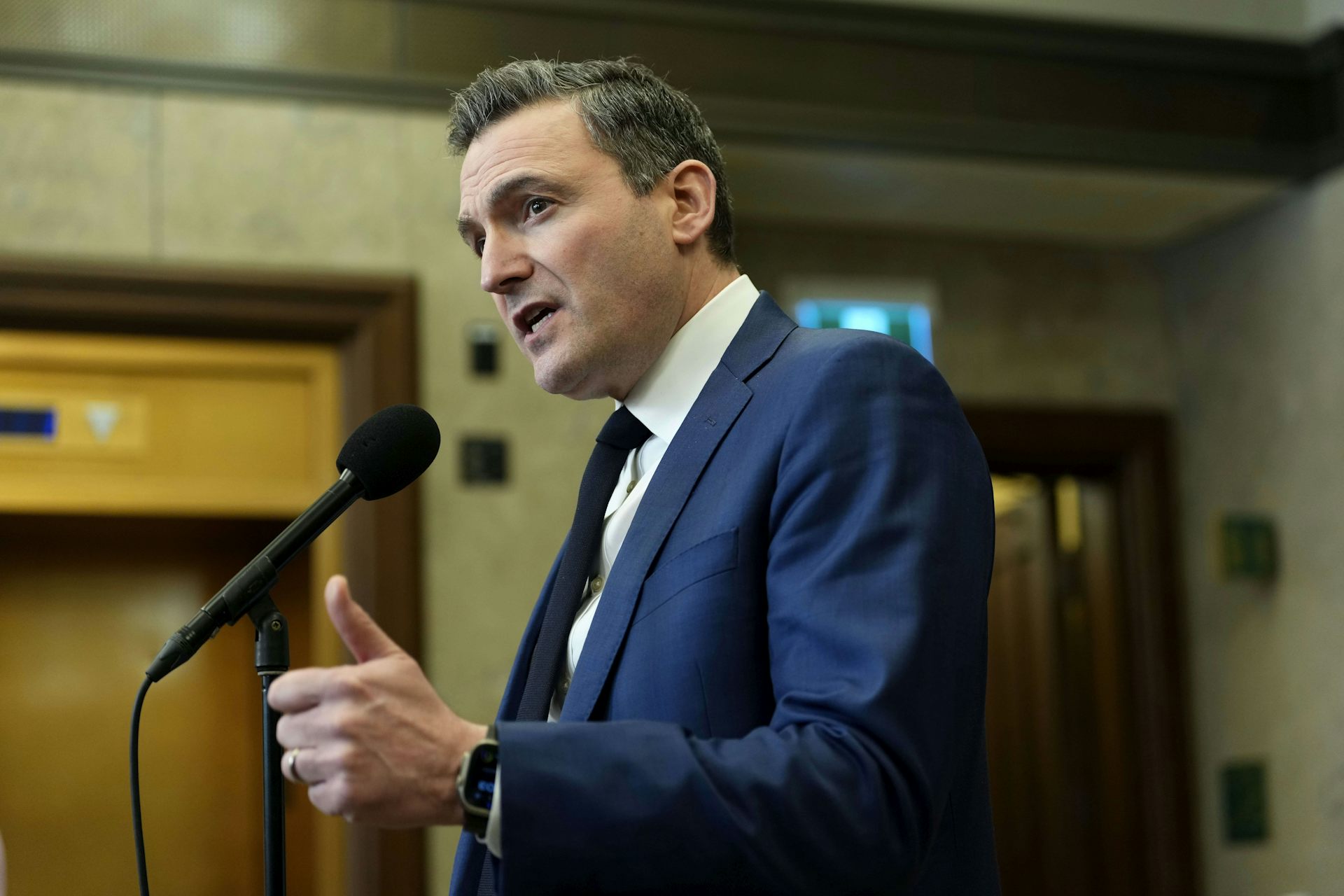 Un hombre de pelo oscuro y traje azul habla por un micrófono.