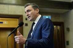 Un hombre de pelo oscuro y traje azul habla por un micrófono.