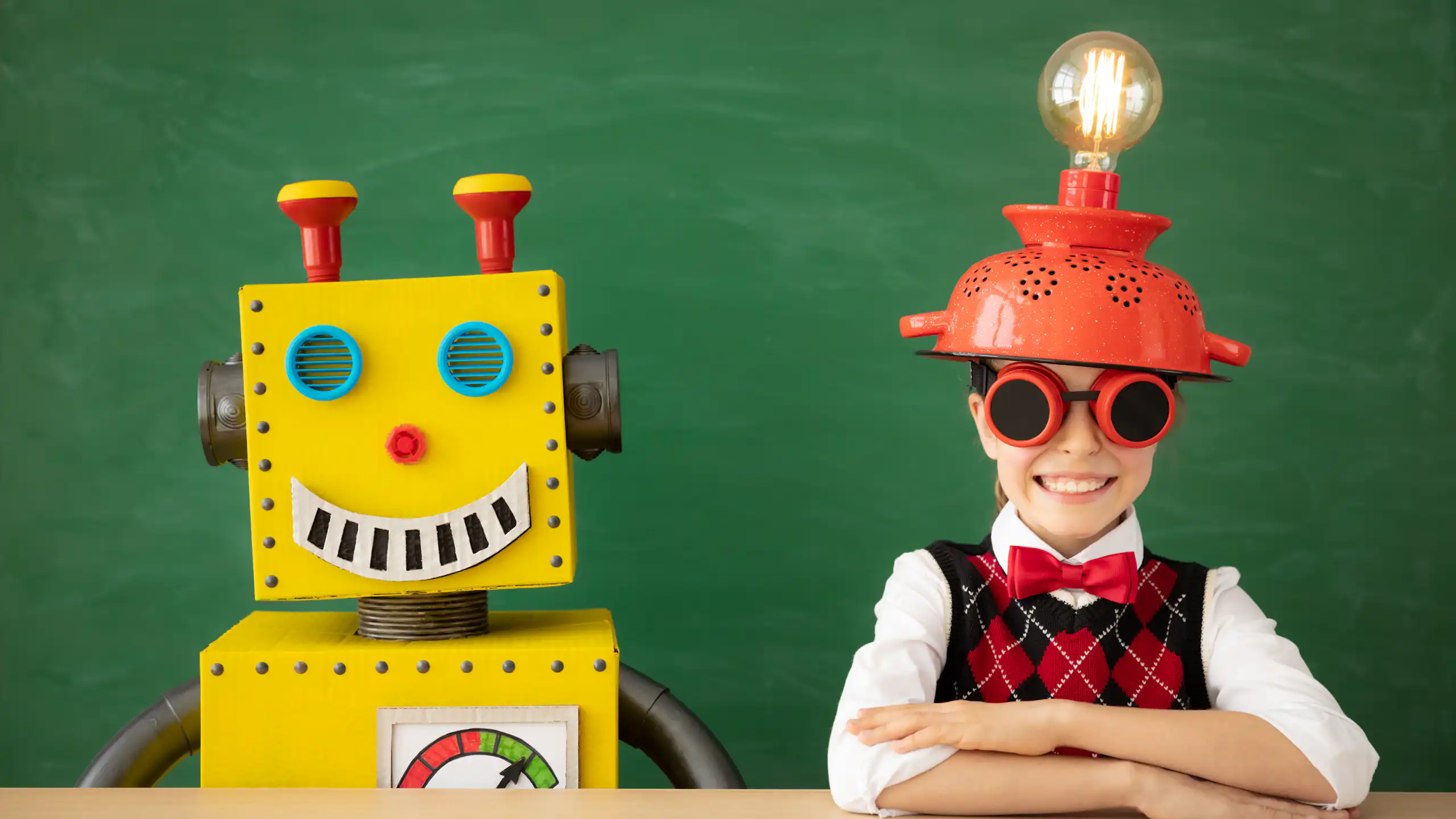 Una nena asseguda al costat d'un robot de cartró, tots dos somrients.