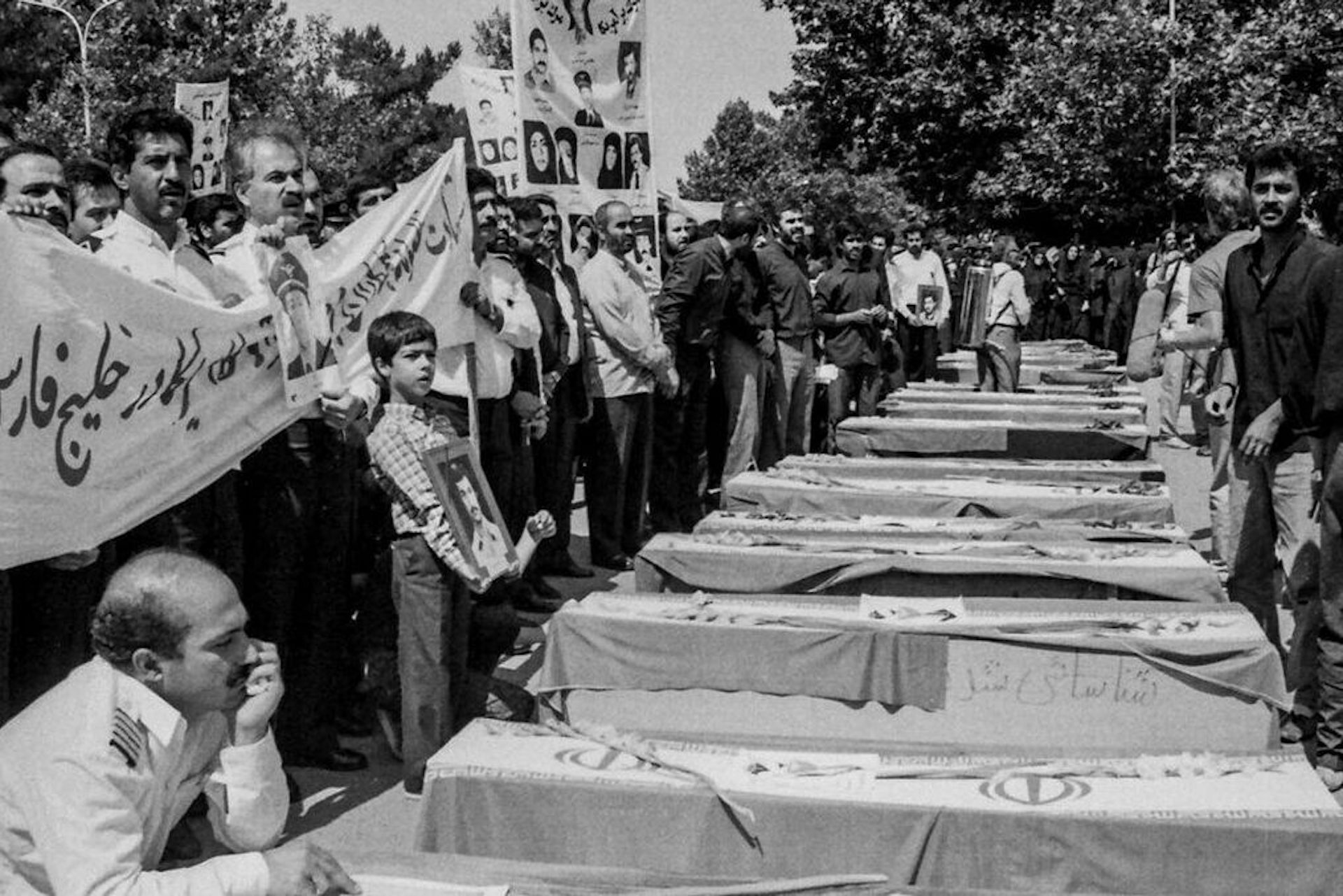 Personas con banderas, pancartas y fotografías junto a una fila de ataúdes