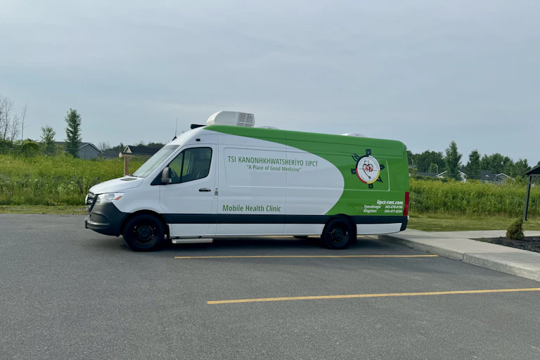 A large green and white van housing a mobile health clinic in a parking lot