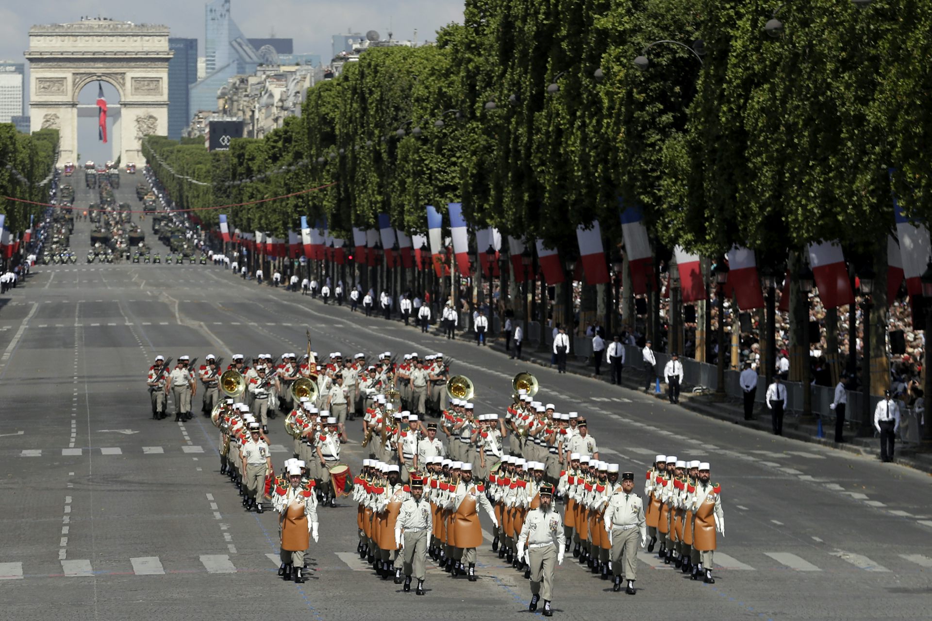 Desfile militar con un gran arco de piedra al fondo.