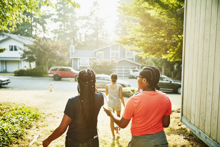 Young women walk toward a sunlit neighborhood street.