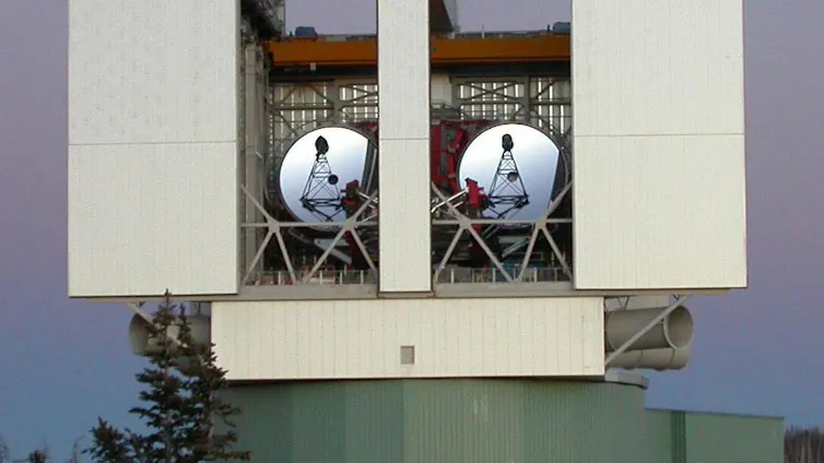 A telescope on a mountaintop set in a box with two antenna disks