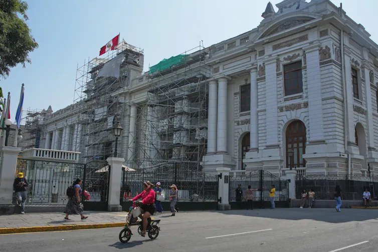 a white building with scaffolding. a Peruvian flag flies above.
