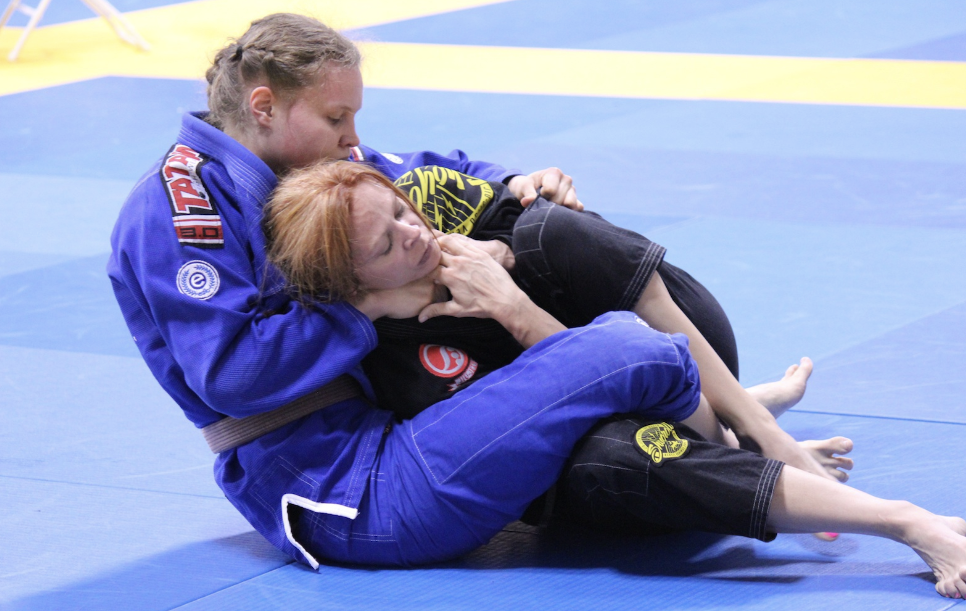 Two young women grappling on a blue mat.