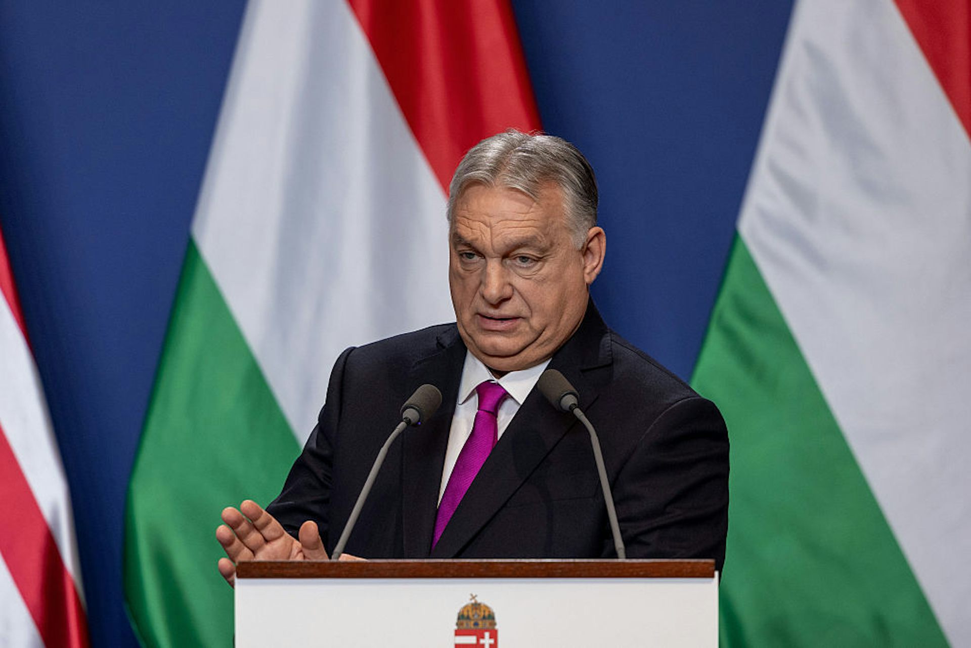 Viktor Orban speaking at a podium in front of the Hungarian flag