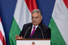 Viktor Orban speaking at a podium in front of the Hungarian flag
