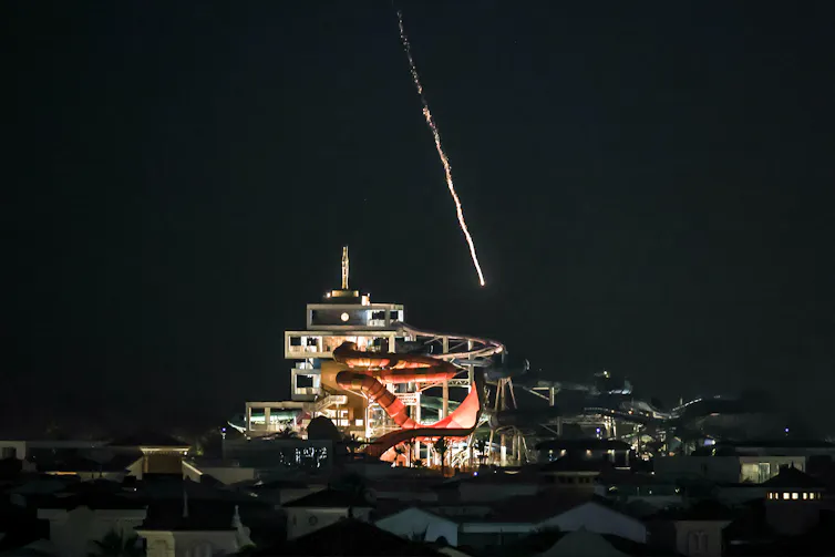 an entertainment building can be seen as a missile falls from the night sky, leaving a trail