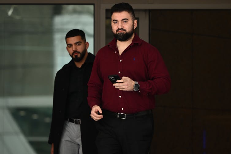A man in a dark red shirt walks out of a court building