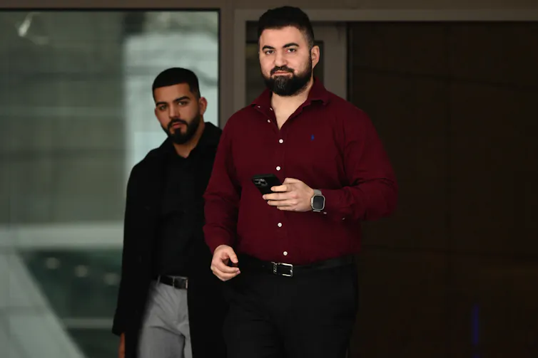 A man in a dark red shirt walks out of a court building