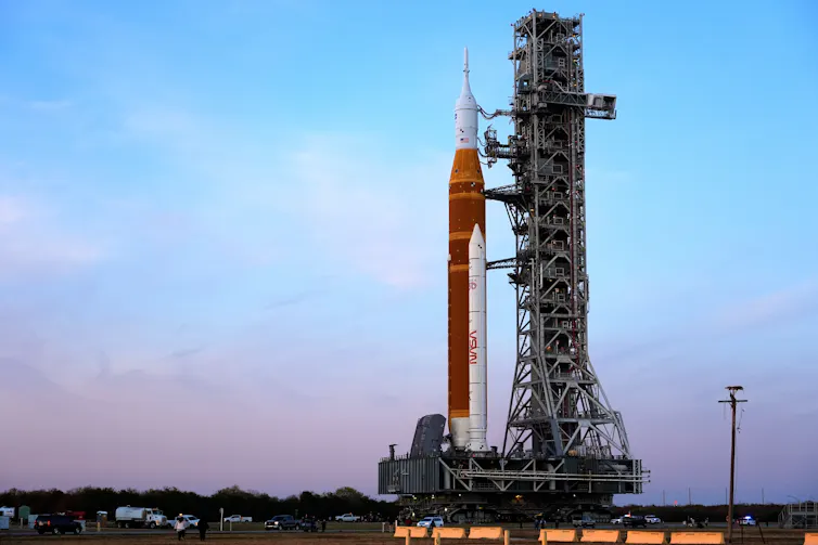 A rocket attached to scaffolding on a rolling pad, against a sunset.