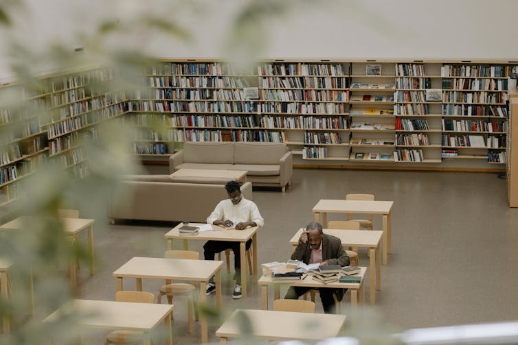 Two people sit at tables in a library.